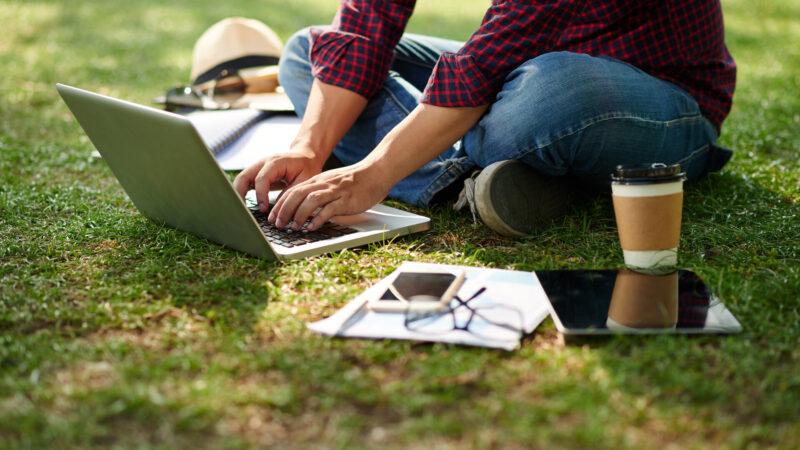 Student, der auf einer Wiese sitzt und am Laptop arbeitet