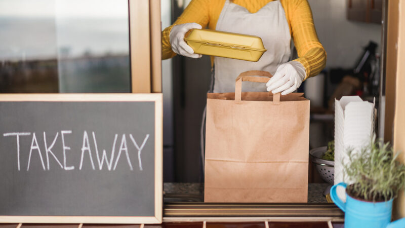 Junge Frau, die Bio-Lebensmittel zum Mitnehmen im Restaurant zubereitet und das Essen in eine Box für unterwegs einpackt