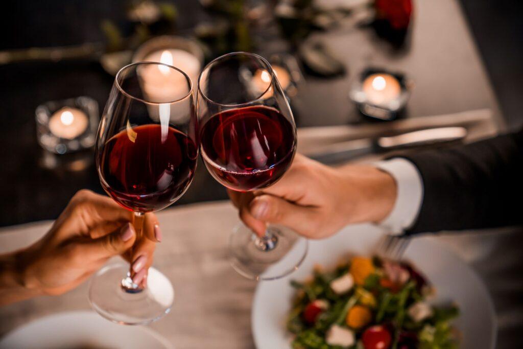 Nahaufnahme eines jungen Paares, das in einem Restaurant mit einem Glas Rotwein anstößt 