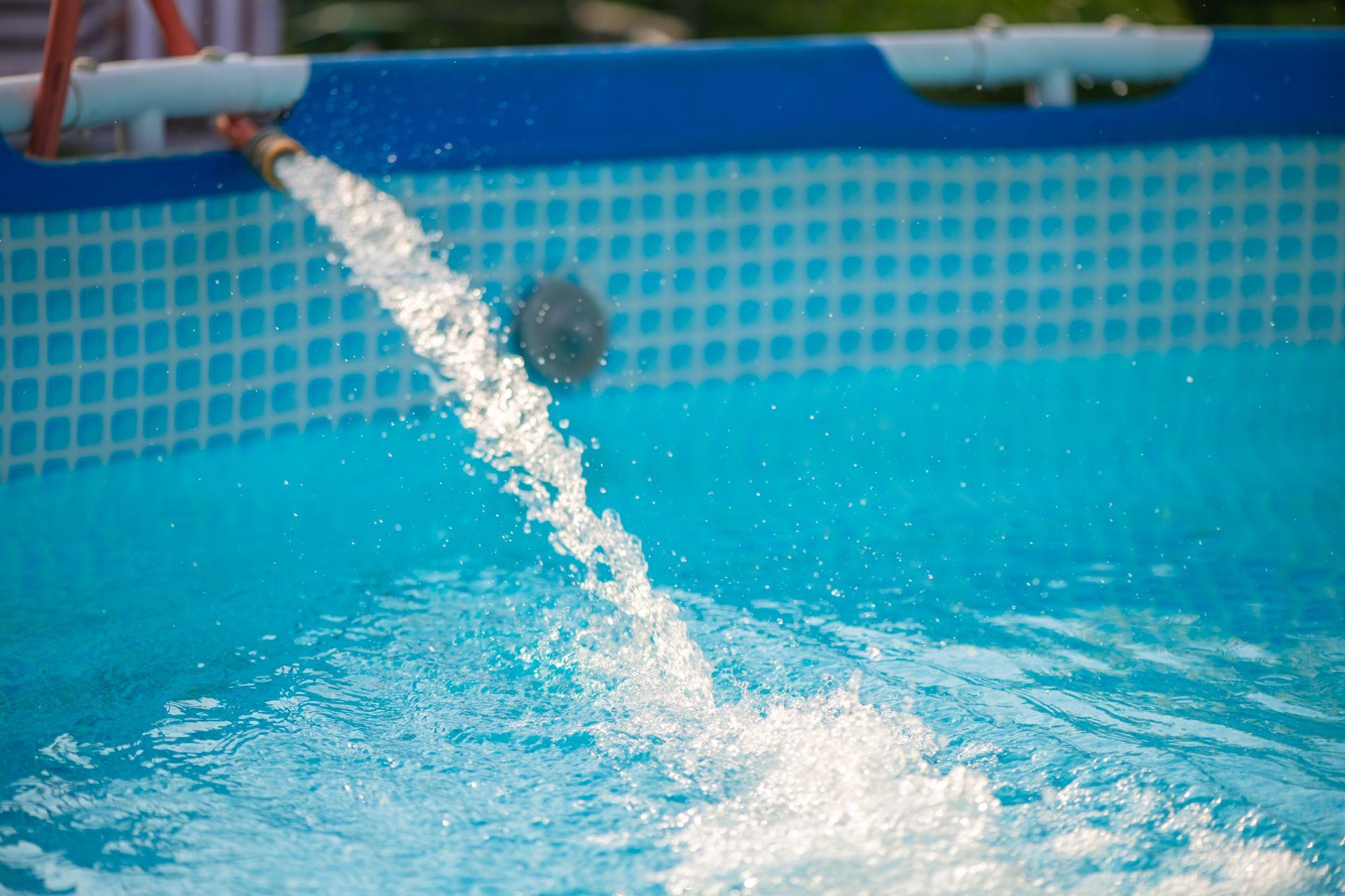 Ein Pool wird mit Wasser befuellt, das durch einen Gartenschlauch in das Becken fliesst – Detailaufnahme aus dem Selbstaufbau